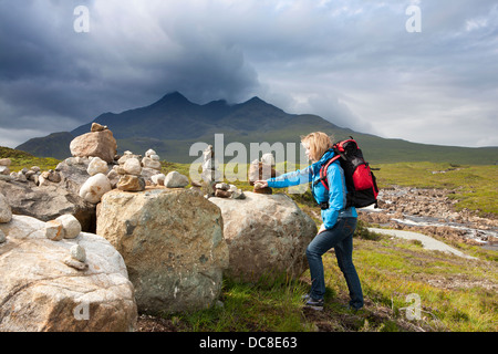 Walker l'ajout en tenant des pierres pour le Scottish Cairns ; memorial Cullin montagne paysage à Sligachan valley sur l'île de Skye, Écosse, Royaume-Uni Banque D'Images