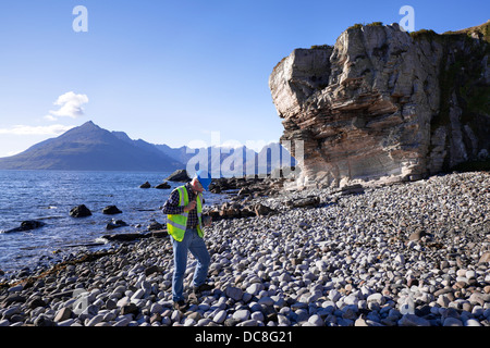 Un géologue sur la plage de galets et sur le rivage d'Elgol.Les collines de Cuillin et les montagnes traversant le Loch Scavaig jusqu'au Loch Coruisk, en Écosse, au Royaume-Uni Banque D'Images