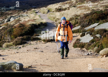 Femme walker en vêtements d'hiver marche sur Pennine Way, sur l'extrémité sud de Kinder Scout, Derbyshire Peak District, UK Banque D'Images