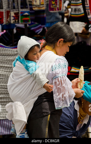 L'Equateur, Quito. Marché d'Otavalo. Jeune mère en tenue traditionnelle highland avec son bébé sur son dos. Banque D'Images