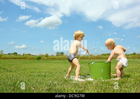 Un jeune enfant et son petit frère jouent à l'extérieur un jour d'été avec un seau d'eau savonneuse, lancer de bulles. Banque D'Images