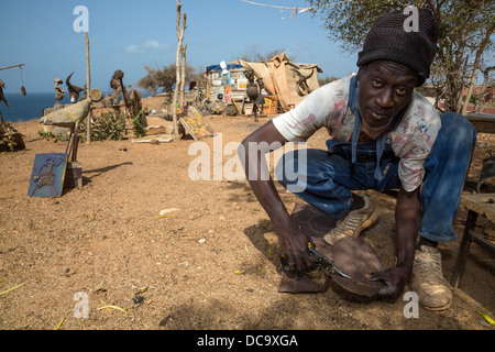 Artiste Amadou Dieng démontrant comment il travaille avec des objets trouvés et récupérés pour faire ses constructions. L'île de Gorée au Sénégal. Banque D'Images