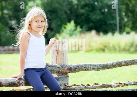 Timide caucasien enfant assis sur clôture de journée ensoleillée. Copyspace village russe. Peuple russe en Russie campagne Banque D'Images