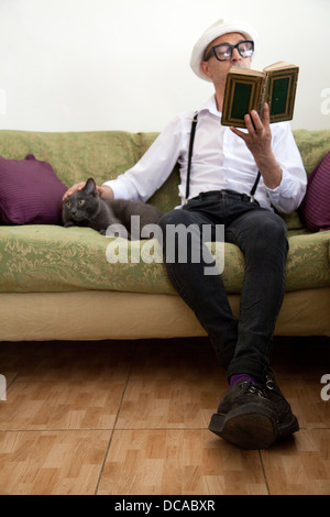 Man reading Book avec Cat on Couch Banque D'Images