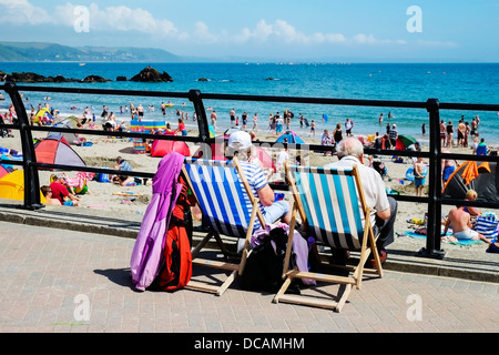 En Looe Cornwall - Les vacanciers assis dans des chaises longues donnant sur une longue plage de Looe est bondé et Cornwall UK Banque D'Images