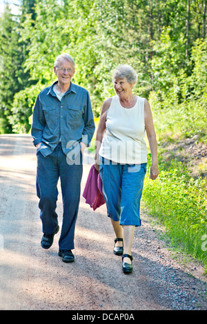 Hauts smiling couple walking on country lane en été Banque D'Images