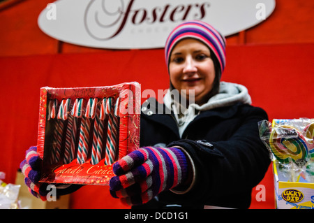 Une jeune femme nous tend un fort de cannes de bonbon at a market stall Banque D'Images