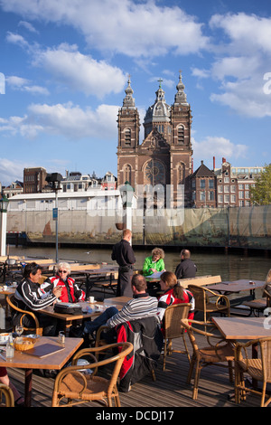 Les touristes en train de déjeuner dans un café restaurant au bord du canal à Amsterdam, Pays-Bas, St Nicholas Church dans l'arrière-plan. Banque D'Images