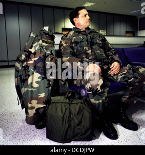 Entouré d'effets personnels et de bagages, un aviateur américain avec l'insigne d'un sergent-chef (CMSgt), attend son vol à la borne de Mildenhall Air Force Base, Suffolk, Angleterre. Banque D'Images