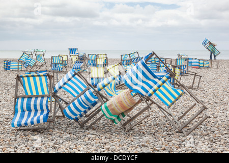 La collecte de l'homme des vents violents les chaises sur la plage de galets de Beer, Devon. Banque D'Images