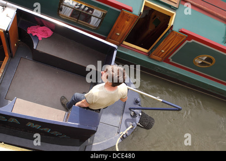 Canal Boat man en utilisant les talles du gouvernail sur un bateau étroit UK Banque D'Images
