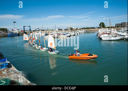 La classe Optimist bateaux à voile remorqué à travers le port de Saint Vaast Normandie France Banque D'Images