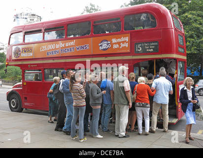 Un groupe de touristes, faisant la queue avec enthousiasme pour monter à bord d'un bus à impériale rouge emblématique de Londres Routemaster , Grande-Bretagne classique Banque D'Images