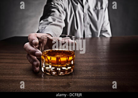 Main d'un homme atteint d'un verre de whisky, qui se dresse sur une table. Banque D'Images