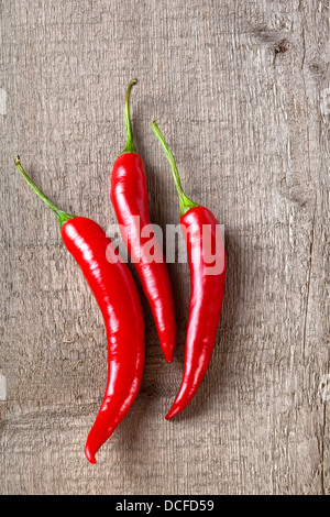 Piments rouges sur fond rustique - trois piments rouges sur une planche ou un fond rustique. Banque D'Images