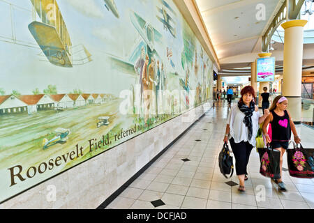 Garden City, New York, USA. 15 août 2013. À Roosevelt Field Mall, une mère et sa fille shopping passe devant un mur peinture murale représentant des scènes de l'aviation le site d'antan. Roosevelt Field est sur le site de renommée mondiale où l'aviateur Charles Lindbergh a décollé pour son vol solo historique à travers l'océan Atlantique à la France en 1927. Le centre commercial est l'un des 10 plus importants aux États-Unis d'Amérique. Banque D'Images