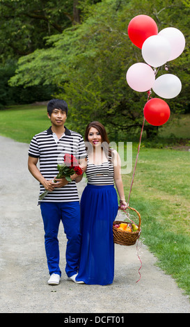 Photo verticale de young adult couple holding balloons, roses rouges et corbeille de fruits tandis que le sentier de randonnée pédestre Banque D'Images