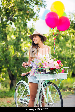 Belle fille en vélo avec des ballons en campagne, vie d'été Banque D'Images