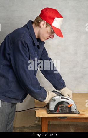 Le travailleur coupe du bois avec une scie circulaire électrique Banque D'Images
