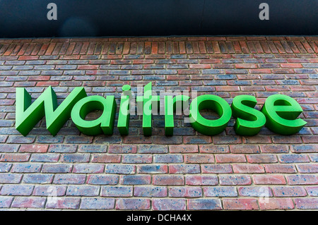 De l'écriture verte familière Waitrose national signe, sur un mur de brique à l'extérieur du village local and Banstead store, Surrey, Angleterre, Royaume-Uni. Banque D'Images