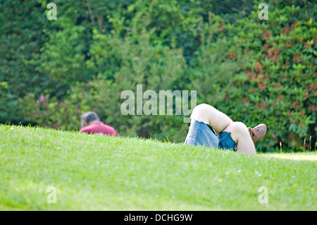 UK park scène, avec quelqu'un est de retour, et une paire de jambes croisées apparaissant de derrière une pente en herbe. Banque D'Images