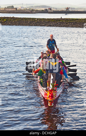 L'équipe de bateau-dragon l'aviron vers la course de départ sur la rivière Irvine, dans le cadre d'Irvine Marymass Festival. Ayrshire du nord Banque D'Images