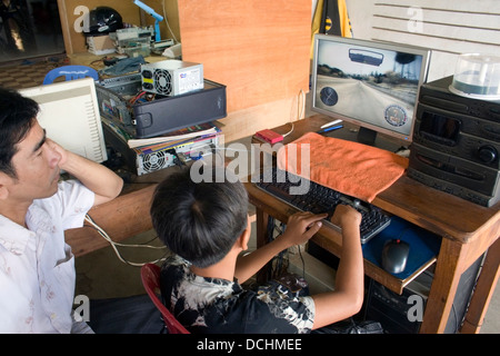 Un homme regarde un jeune garçon de 11 ans jouer un jeu d'ordinateur à Kampong Cham au Cambodge. Banque D'Images