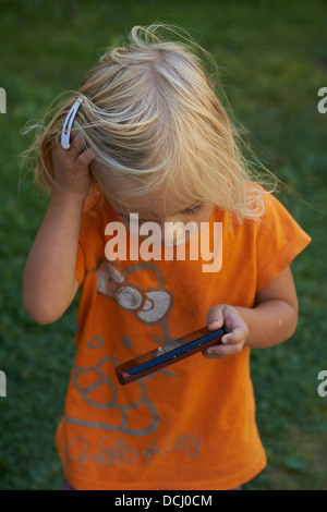 Enfant fille blonde Toddler Playing with cell phone outside Banque D'Images