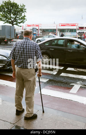 Homme avec bâton de marche en attente de possibilité de contre route occupée à l'extérieur de l'Ermitage à Saint-Pétersbourg, Russie Banque D'Images