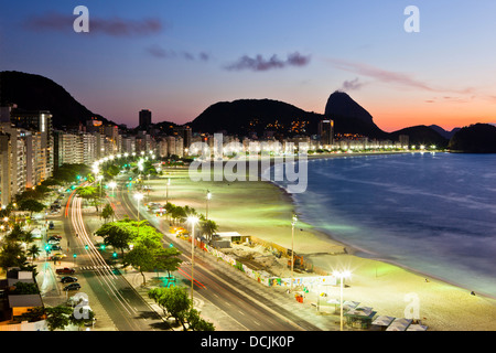 Lever du soleil sur la plage de Copacabana, Rio de Janeiro, Brésil. L'avenue Atlantica, mont du Pain de Sucre en arrière-plan. Banque D'Images