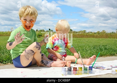 Deux professionnels de jeunes enfants, un petit garçon et petit frère, sont assis dehors sur une journée d'été la peinture d'une photo et d'eux-mêmes Banque D'Images