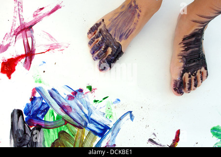 Close up sur un petit pieds de l'enfant qui sont couverts dans la peinture, debout sur un grand papier blanc vierge de peintures colorées Banque D'Images