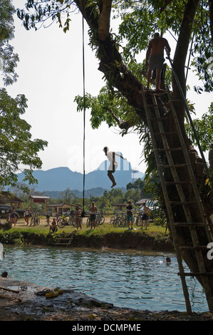 Vue verticale d'un touristiques sautant d'un arbre dans le bleu lagon, le long de la rivière Nam Song près de Vang Vieng. Banque D'Images