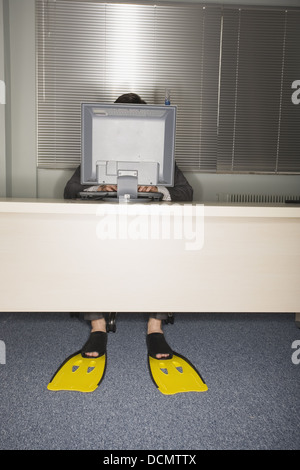 Employée de bureau à l'ordinateur portant des palmes de natation Banque D'Images