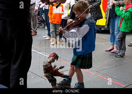 Édimbourg, Écosse, 20 août 2013, Colin McGlynn de Virginie aux États-Unis à l'âge de 7 ans pourrait être le plus jeune musicien ambulant sur le Royal Mile, au cours de l'Edinburgh Fringe Festival 2013. Il a diverti les passants en jouant des airs écossais sur son violon ainsi que la réalisation avec Mojo de JP Puppets Banque D'Images