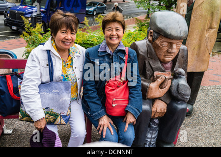 Les touristes asiatiques posant avec un immense, plus grand que nature, groupe de sculptures en bois à St John, Nova Scotia, Canada. Banque D'Images