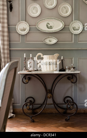 Assiettes décoratives accrochées sur les panneaux de mur en bois recouvert de marbre antique au-dessus d'une table console avec jambes de fer Banque D'Images