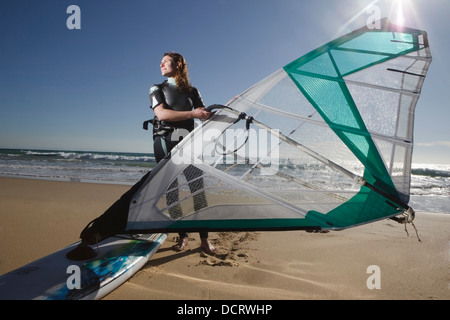 Jeune femme posant avec sa planche à voile sur la plage Banque D'Images