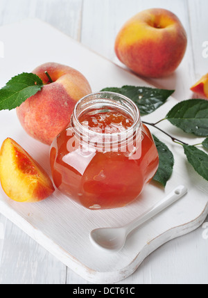 Confiture de pêches dans un bocal en verre sur fond de bois blanc Banque D'Images