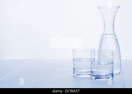 Carafe à eau et 2 verres - une carafe d'eau sur une table avec deux verres, dans les tons bleu, à l'horizontale. Banque D'Images