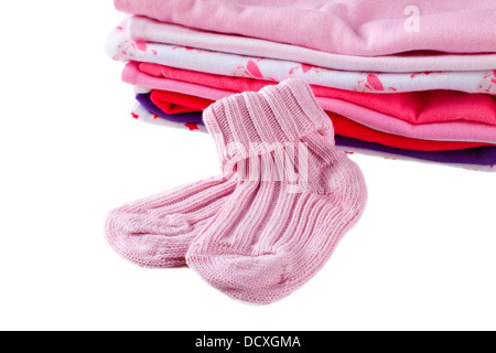 Chaussettes bébé fille rose en face d'une pile de vêtements colorés pour bébé, isolé sur fond blanc Banque D'Images