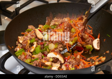 Mélanger le porc avec la friture de légumes dans un wok sur un brûleur à gaz Banque D'Images