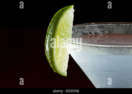 Le quartier de lime sur le bord du verre à cocktail utilisé comme garniture isolé sur un fond noir Banque D'Images