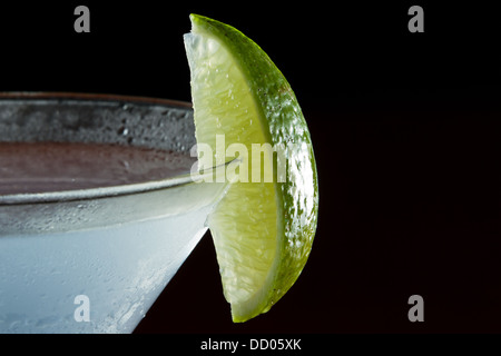 Le quartier de lime sur le bord du verre à cocktail utilisé comme garniture isolé sur un fond noir Banque D'Images