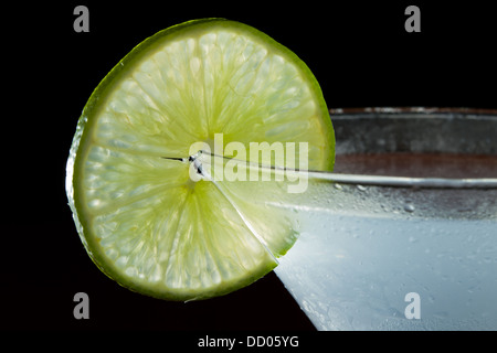 Roue de lime sur le bord du verre à cocktail utilisé comme garniture isolé sur un fond noir Banque D'Images