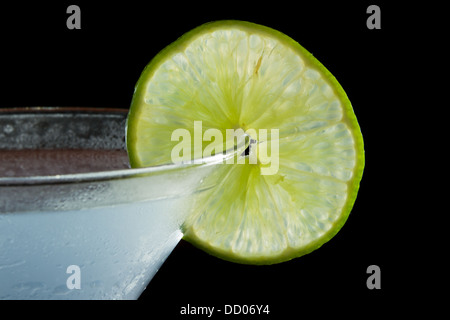 Roue de lime sur le bord du verre à cocktail utilisé comme garniture isolé sur un fond noir Banque D'Images