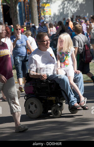 Père débarrasser fauteuil roulant motorisé avec fille à cheval sur ses genoux. Minnesota State Fair jour d'ouverture le jeudi 22 août 2013 St Paul Minnesota MN USA Banque D'Images