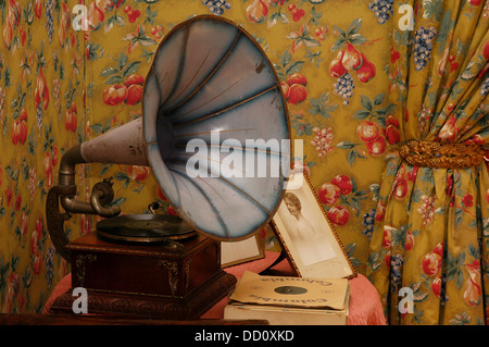 Ancien gramophone à manivelle portable haut-parleur dans la salle de séjour avec une décoration papier peint floral Banque D'Images