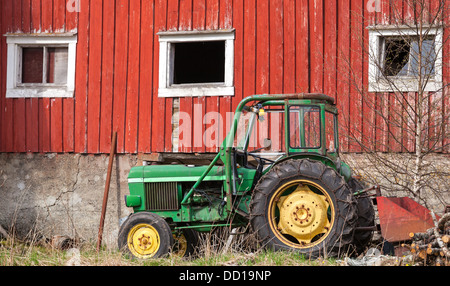 Petit tracteur vert se dresse sur l'herbe rouge à proximité de mur de la grange en Norvège Banque D'Images