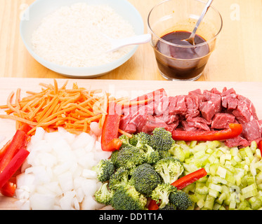 Ingrédients sauté de boeuf sur une planche à découper avec du riz et de la sauce soja en arrière-plan Banque D'Images